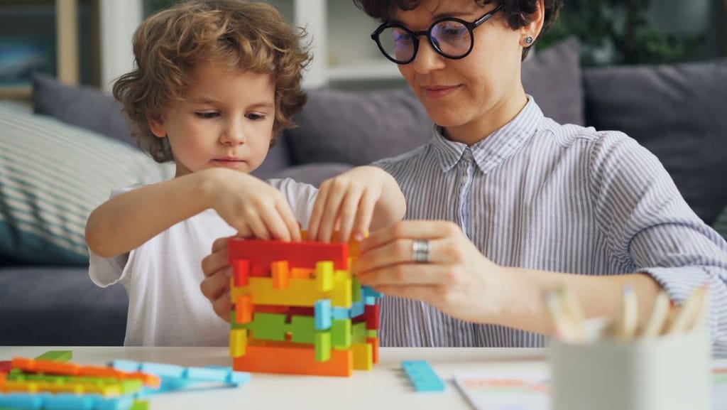 An adult and child building with colorful blocks during a play-based ABA therapy session