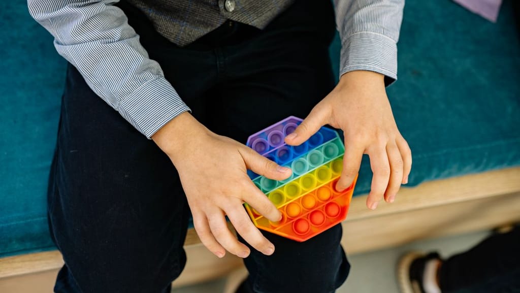 A child holding a rainbow pop-it sensory toy, a common self-regulation tool for autism stimming