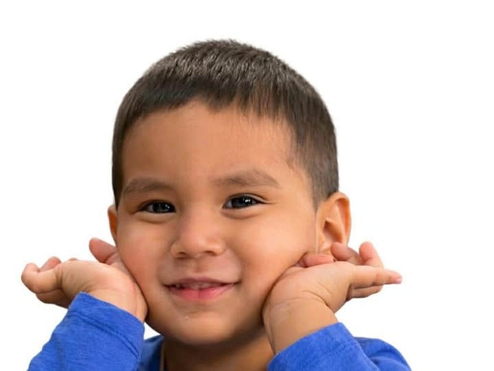 A child in the Autism Resources & Support community A smiling young boy resting his chin on his hands at a table.