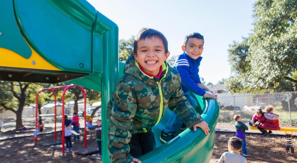 Two Cedars International Academy students using a colorful playground slide outdoors.