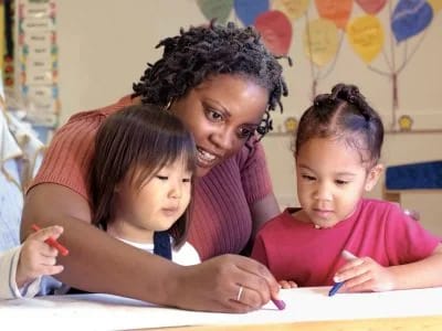 Adult helping two young children with a classroom activity