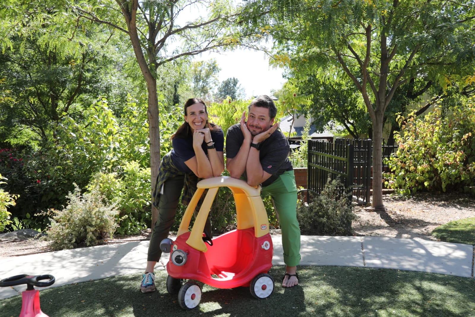 Elizabeth Academy student riding a toy car with two staff members outdoors.