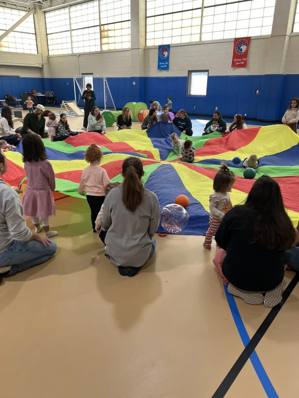 Happy Day Play children and caregivers using a parachute in the gym