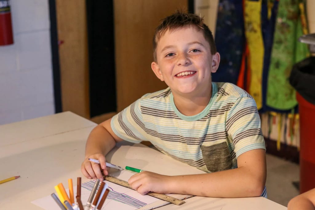 Intermountain Christian School student smiling at a classroom desk with art supplies.