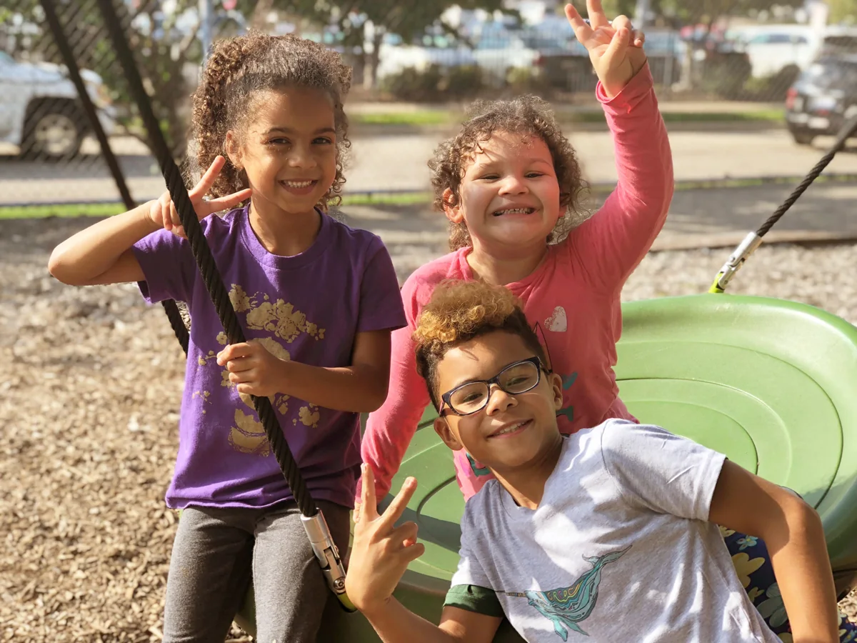 Three Grand Rapids Child Discovery Center students smiling on the playground.