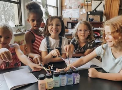 Young Leaves of Learning students gathered around art materials in a classroom.