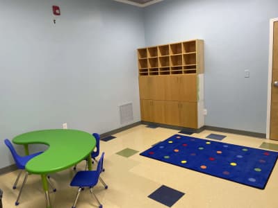 Indoor therapy room with child-sized tables and a colorful activity rug at ABI New England.