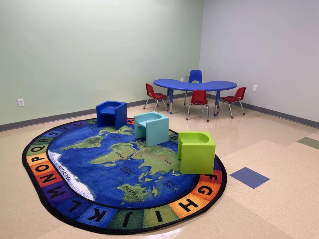 Indoor play area with a colorful activity rug and child-sized seating at ABI New England.