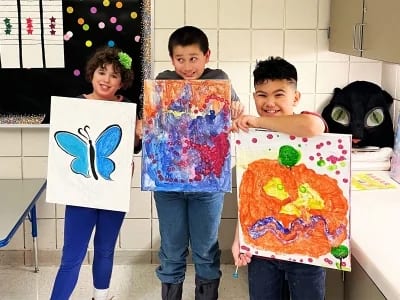 Three Carmen B. Pingree Autism Center students holding colorful paintings.