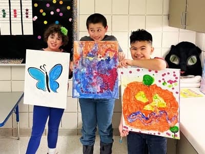 Three Carmen B. Pingree Autism Center students holding colorful paintings.