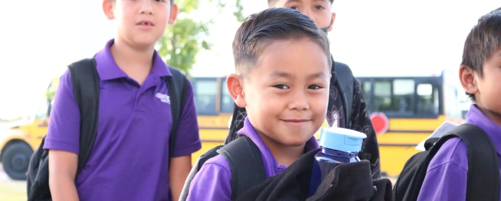 Austin Achieve students with backpacks near a school bus outside the Austin campus.