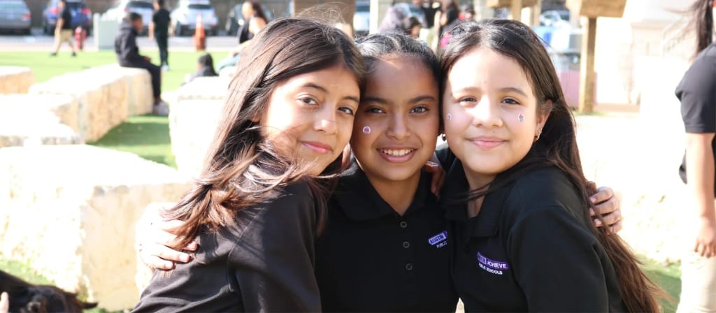 Three Austin Achieve students smiling together outdoors on campus.