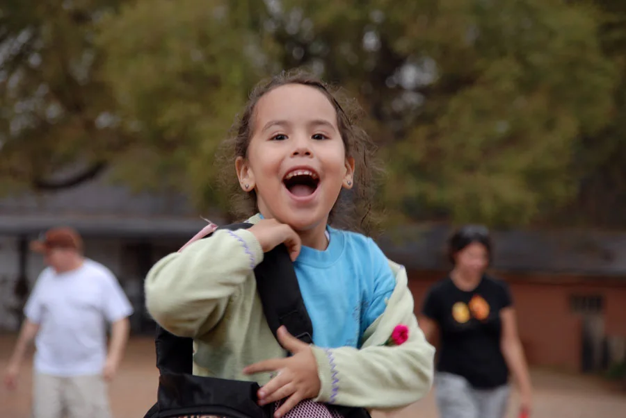 Smiling Albuquerque Sign Language Academy student outdoors with classmates in the background.