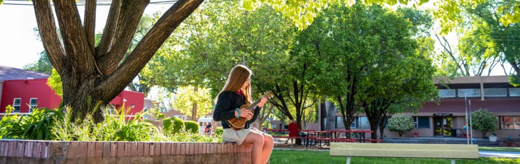 Student seated beneath mature trees in a landscaped courtyard at Menaul School.