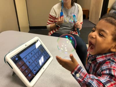 Child using a supported communication device during an activity at i-CAN Children's Therapy.