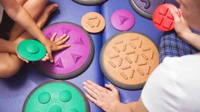 Hands reach toward colorful pieces on a circular tabletop activity board.