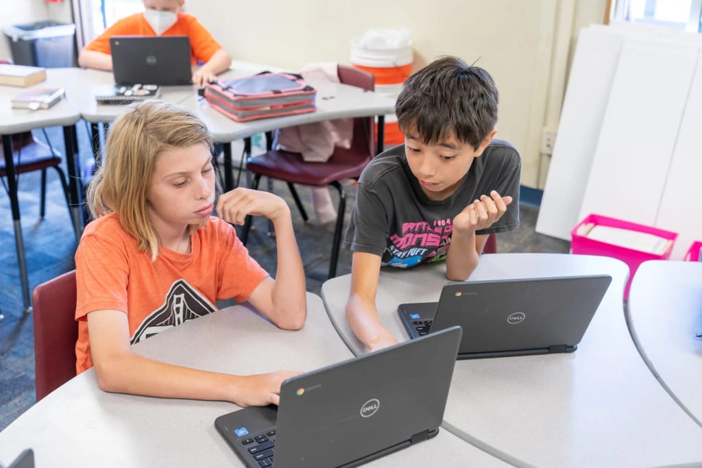 Teach Elementary School students collaborating on laptop-based classroom work.