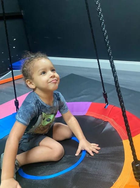 Child sitting on a platform swing in a therapy gym.