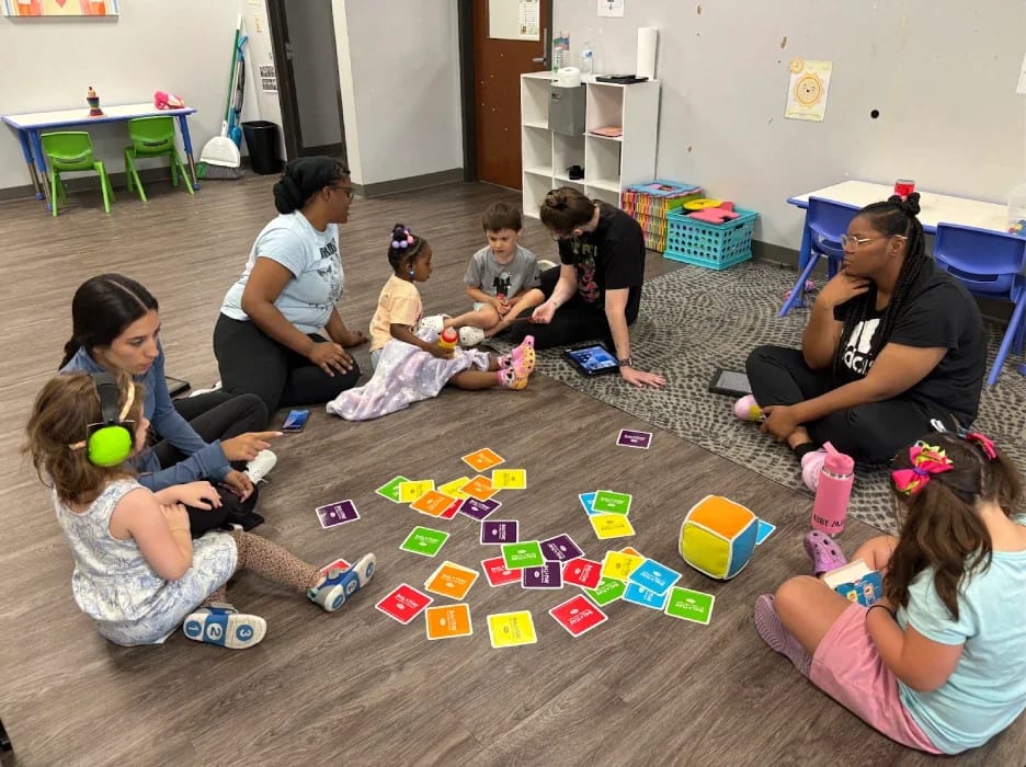 Children and therapists doing a group activity on a therapy room floor.