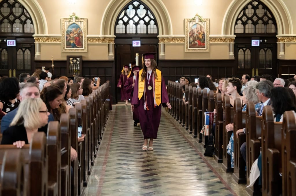 A student walking through a graduation ceremony at Our Lady of Mount Carmel Academy