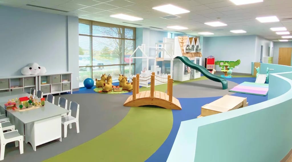 Indoor gross-motor play room with ramps, toys, and seating at Action Behavior Centers.