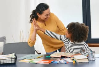 Caregiver and child sharing a high-five at a table with learning materials.