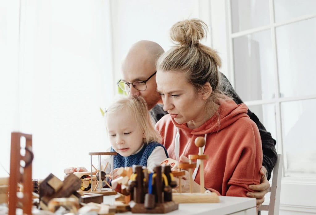 Parents supporting a young child during a play activity at home