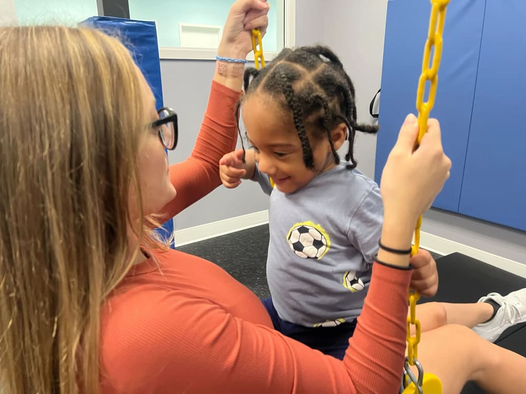 Therapist helping child use indoor sensory therapy swing