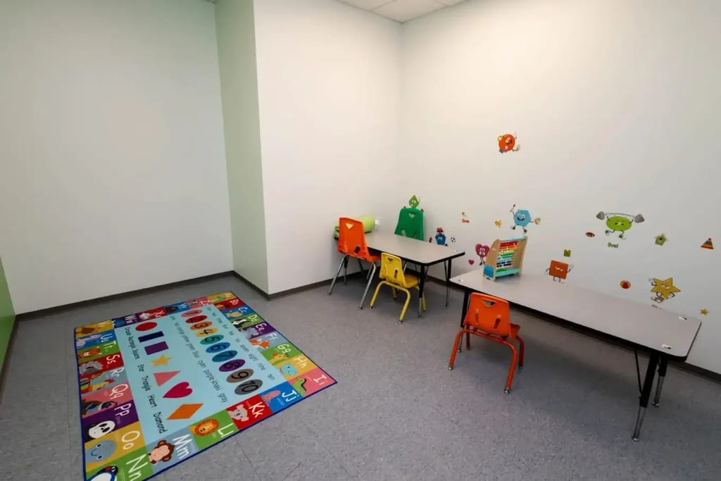 Child-sized learning room with colorful tables, chairs, and an alphabet rug